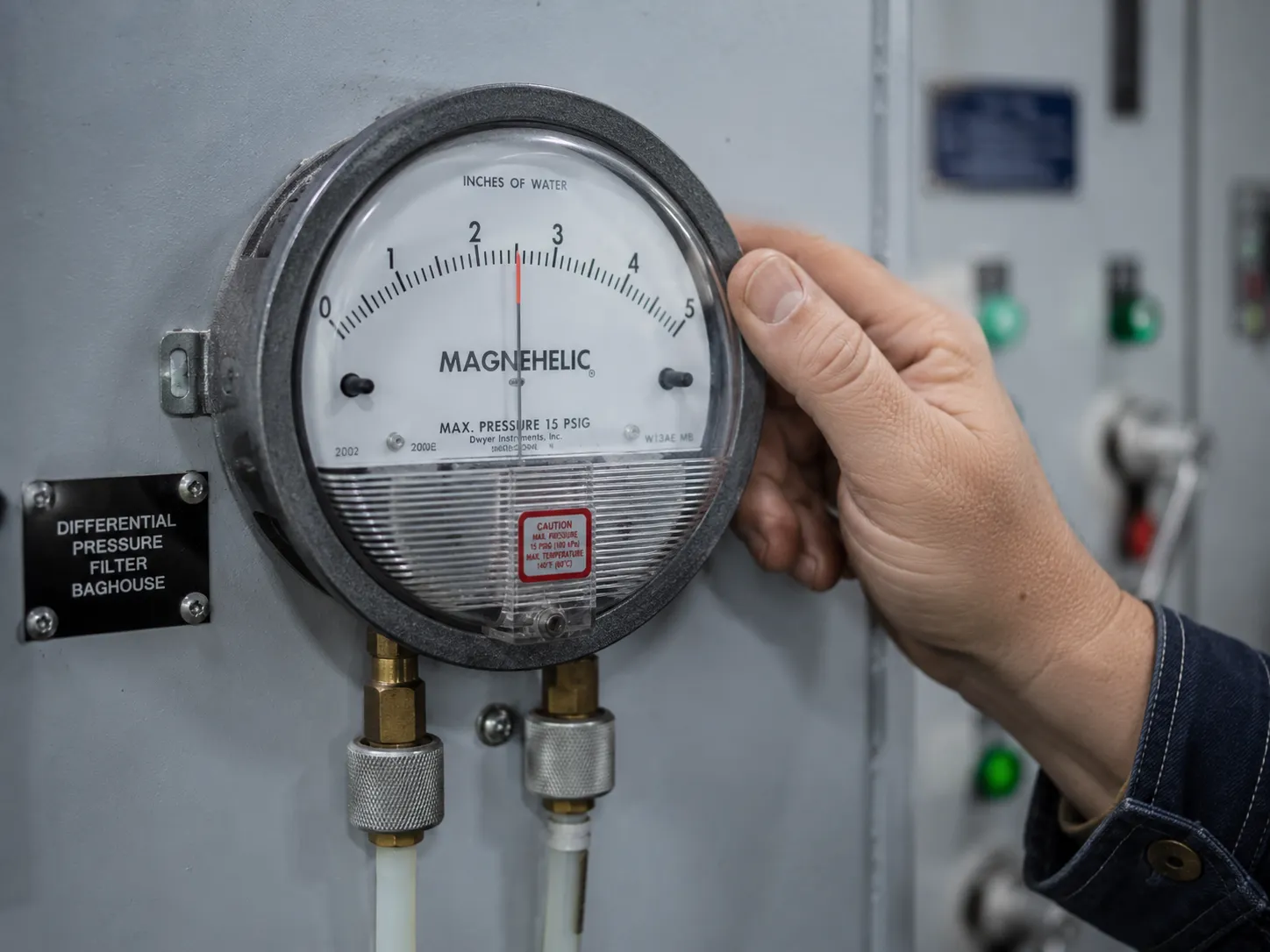 Technician reading a differential pressure gauge on an industrial dust collector.